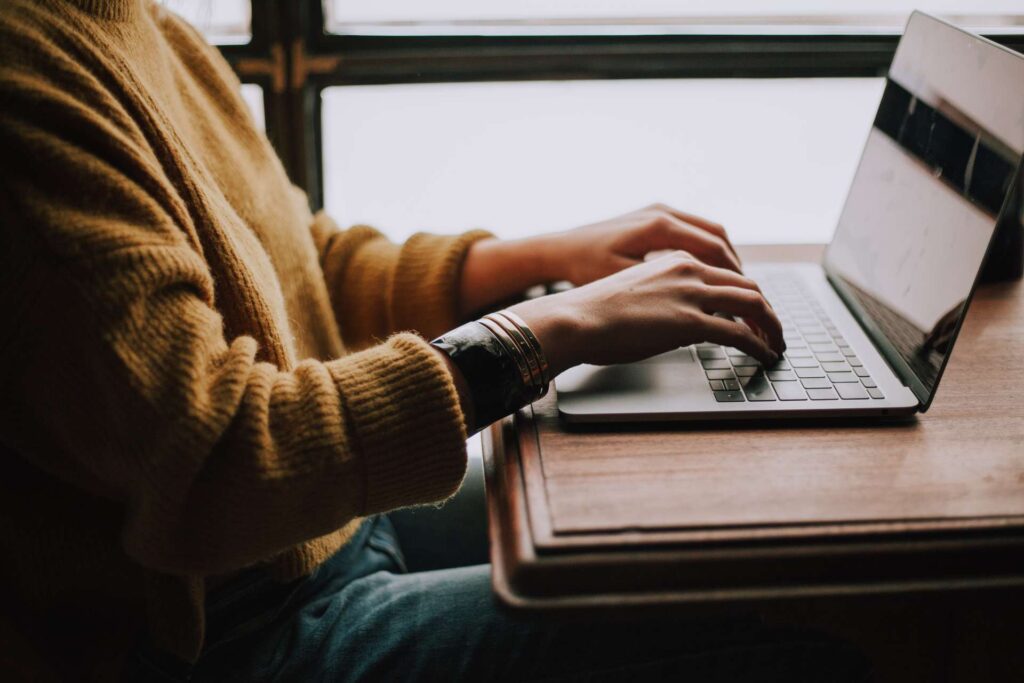 laptop na stolu - osoba sedi ispred laptopa i kuca na njemu - on-page optimizacija