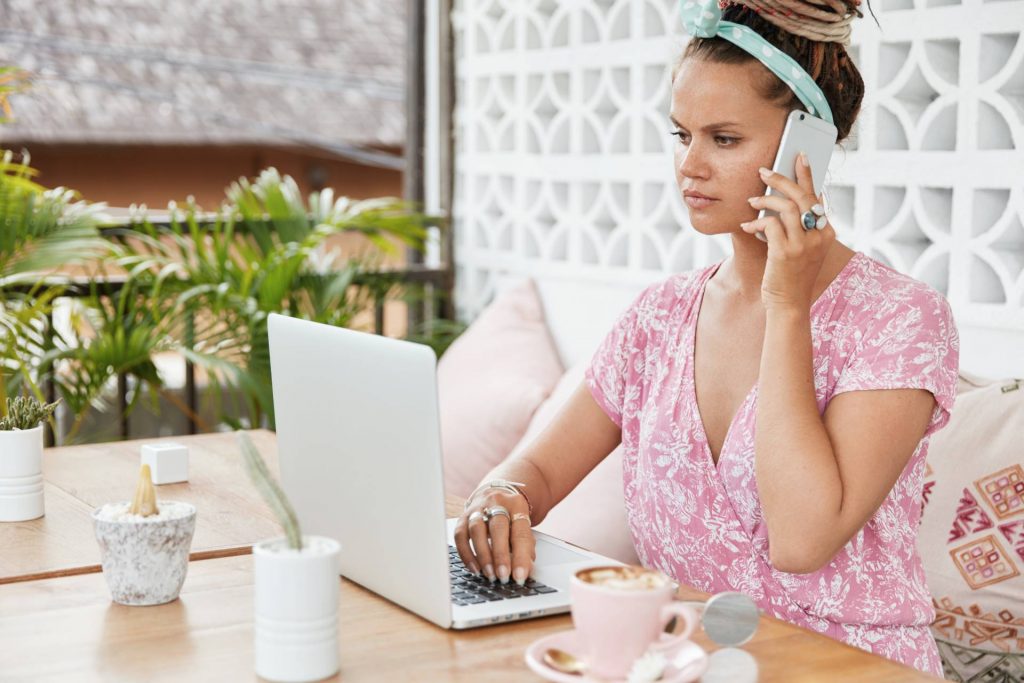 devojka koristi laptop dok prica na telefonu
